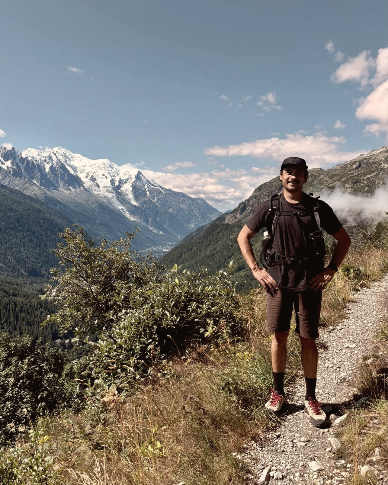 Ken Day standing on a mountain trail above Chamonix, with snow-capped peaks behind.